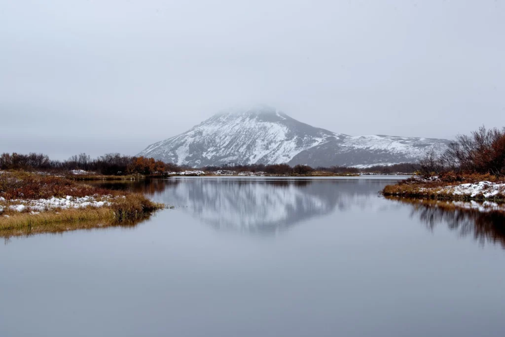 Winterlandschaft mit verschneitem Berg und ruhigem See im Vordergrund.